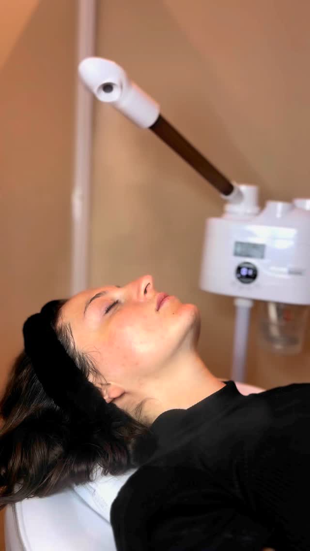 Una clienta con vincha negra, los ojos cerrados, bajo el vaporizador de ozono durante una limpieza facial